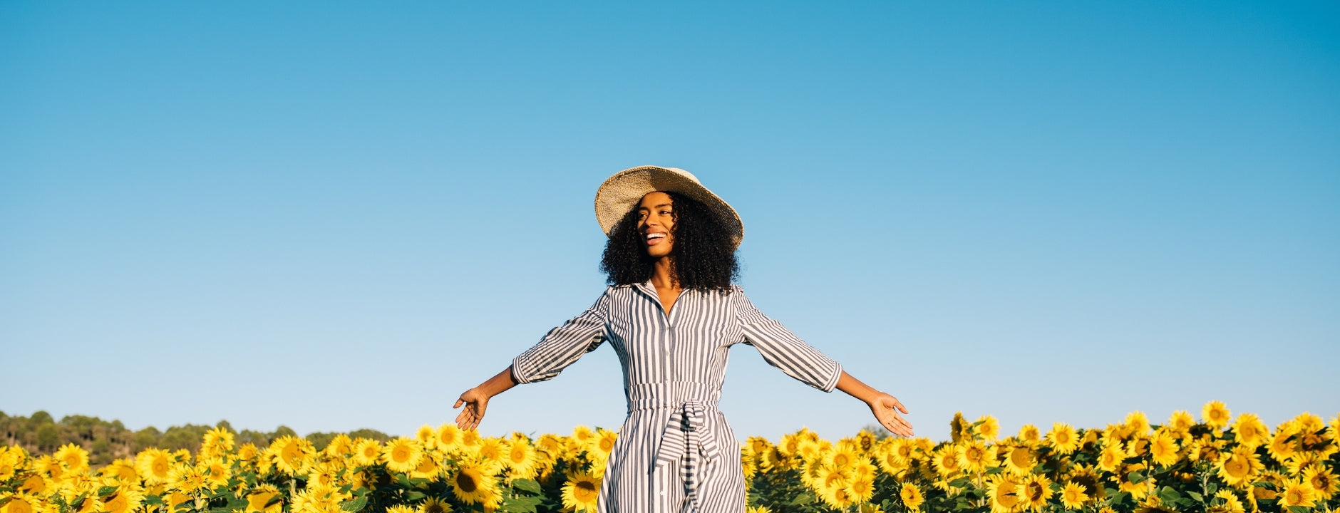 Woman smiling in a sunflower field under a clear blue sky, expressing a sense of serenity and freedom.