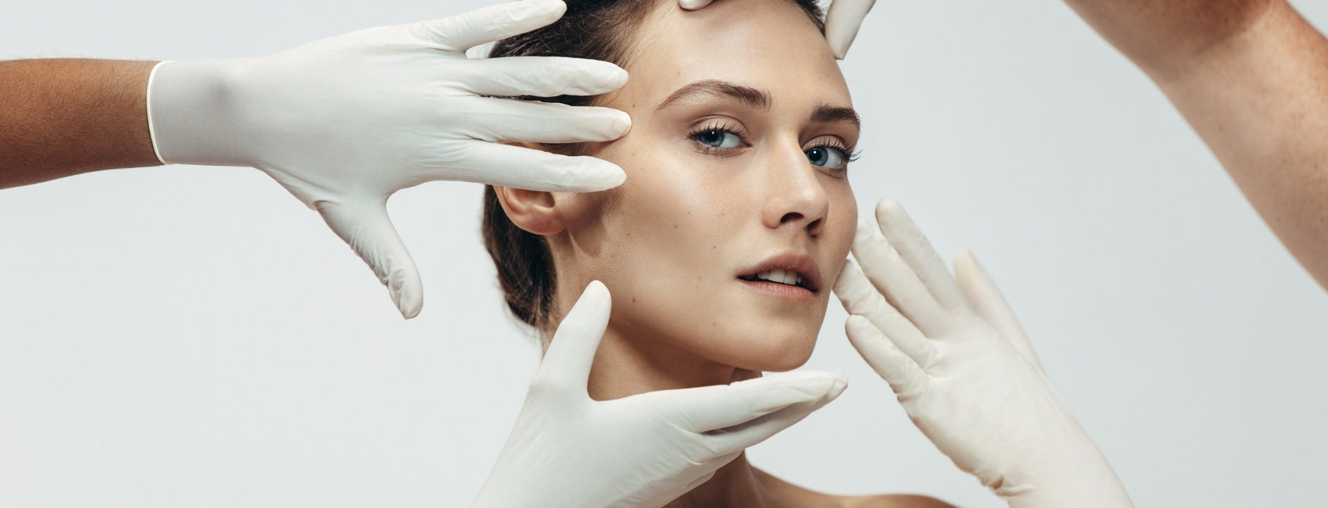 Close-up of a woman’s face framed by gloved hands during a skincare or dermatology treatment, highlighting smooth, radiant skin.