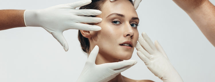 Close-up of a woman’s face framed by gloved hands during a skincare or dermatology treatment, highlighting smooth, radiant skin.