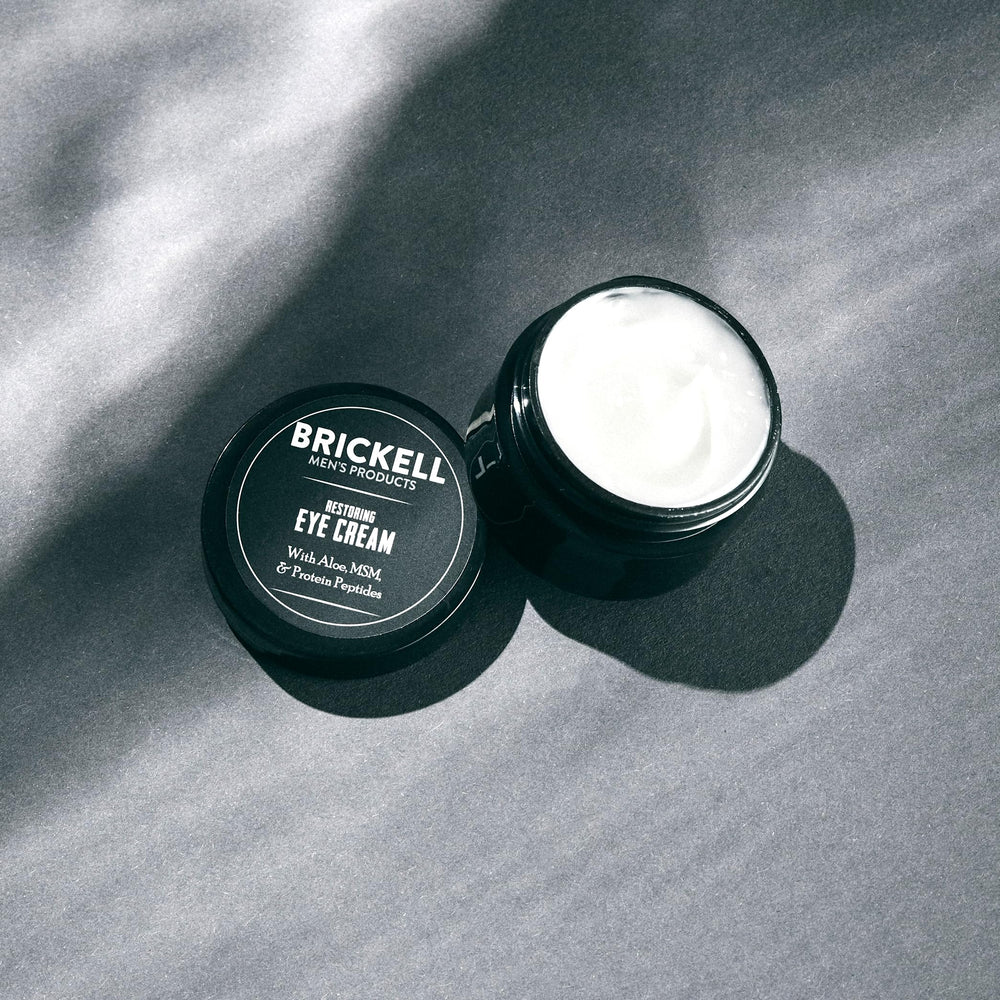 Brickell Men's Restoring Under Eye Cream jar close-up shows green tea and aloe leaves.