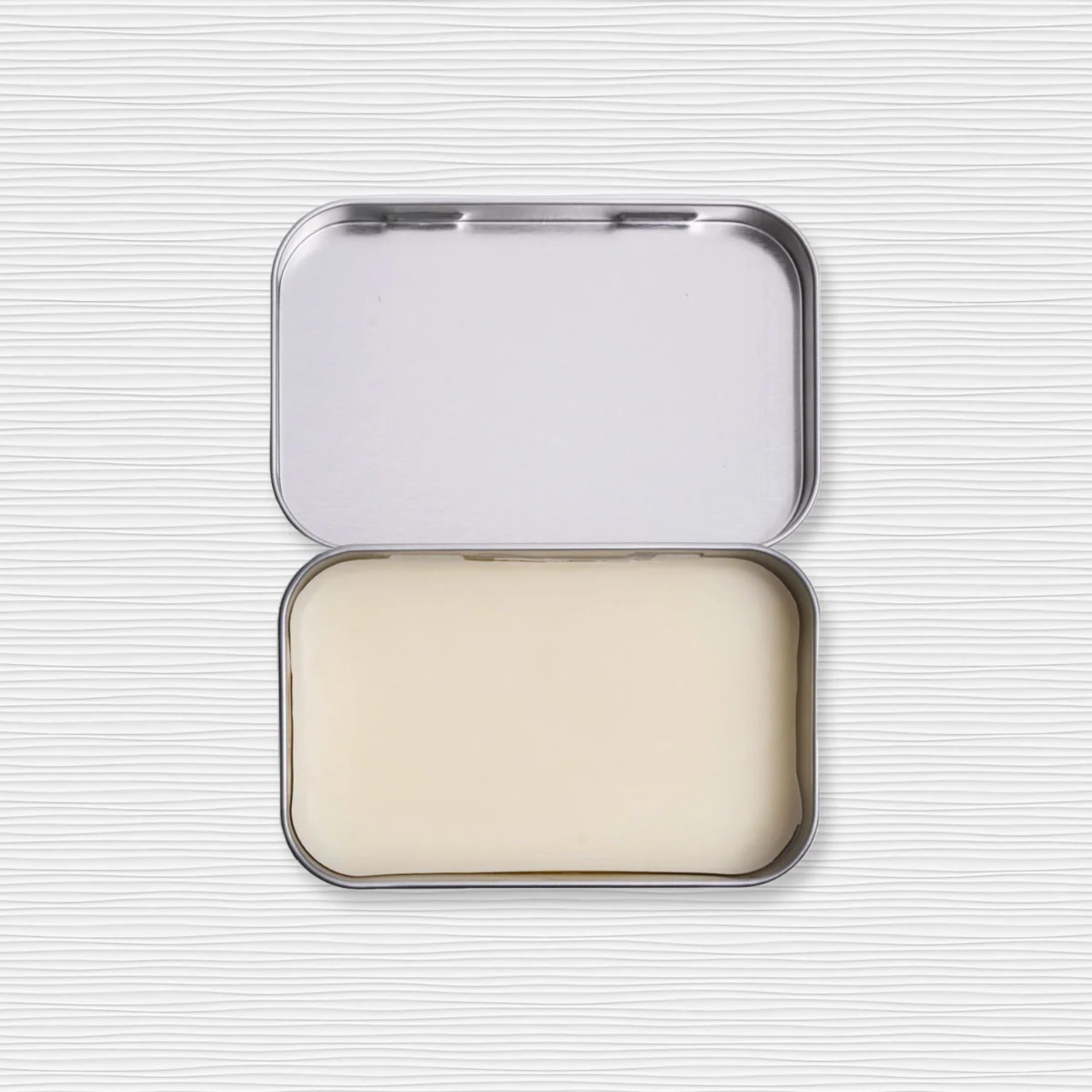 Duke Cannon Old Glory travel tin beside a leather bag for discreet scent refreshes.