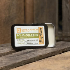 Duke Cannon Bay Rum solid cologne being applied with fingertip for precision scent.