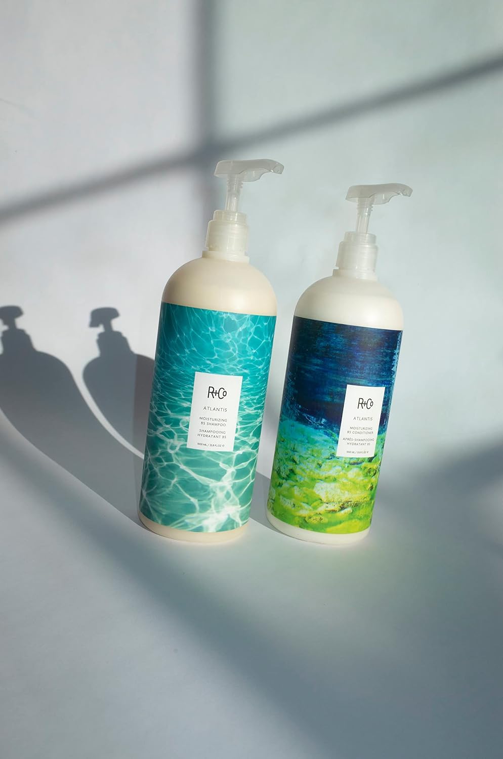 R+Co Atlantis conditioner bottle with glass of water background signaling hydration