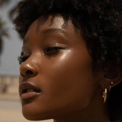 Tower 28 SuperDew balm applied to cheekbone for natural radiance.