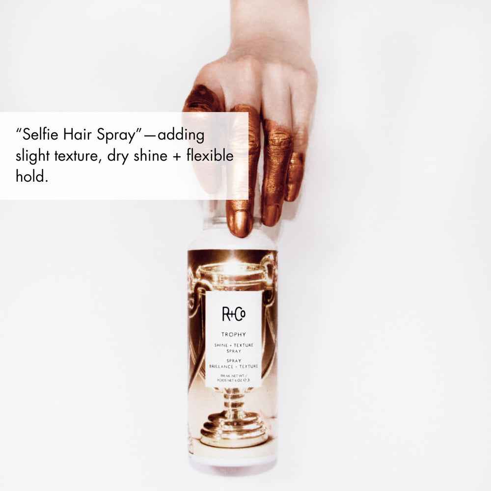 R+Co Trophy Shine Texture Spray bottle on mirror, ready for refresh.