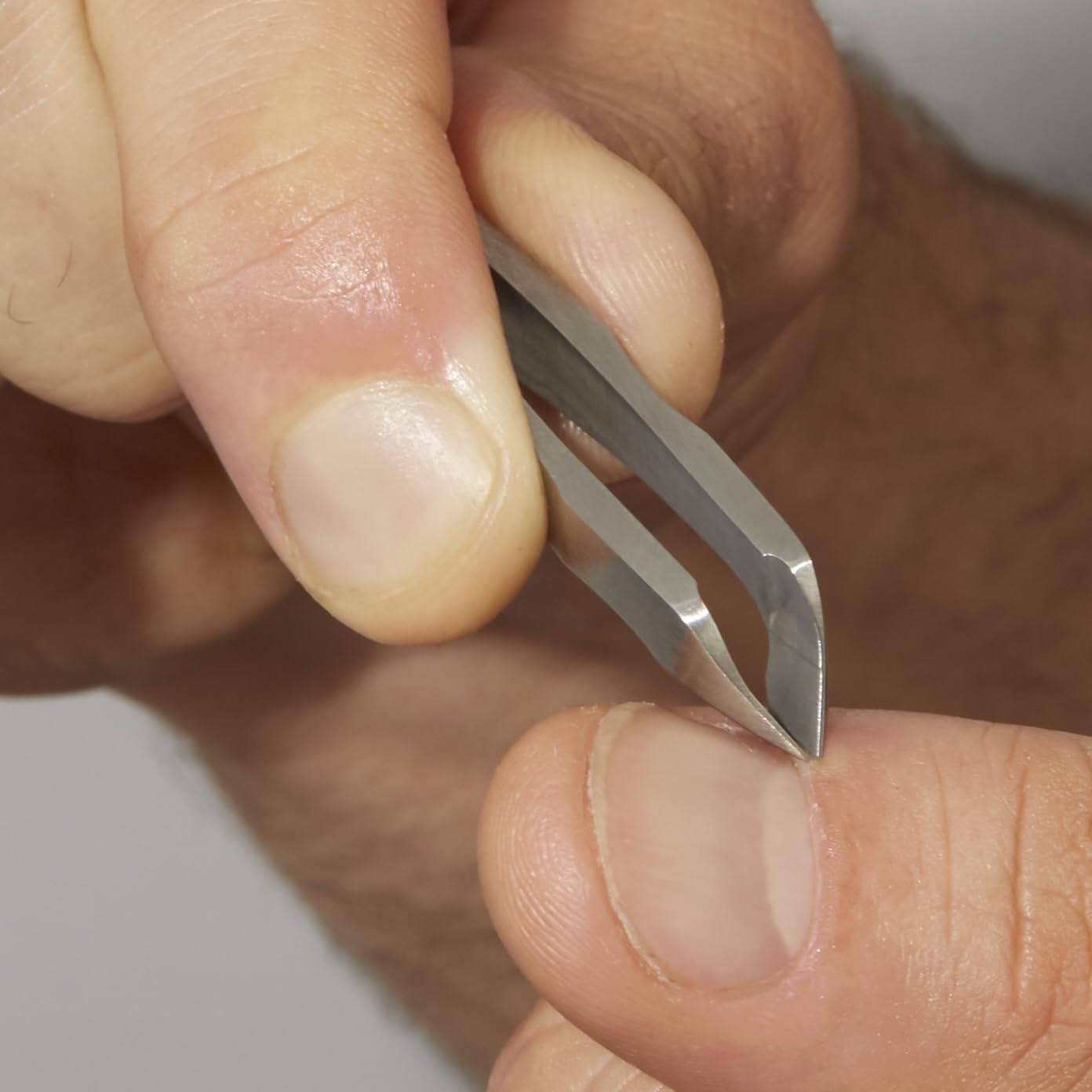 Tweezerman Mini Squeeze Cutical Nipper silver in-use action showing precise trimming.